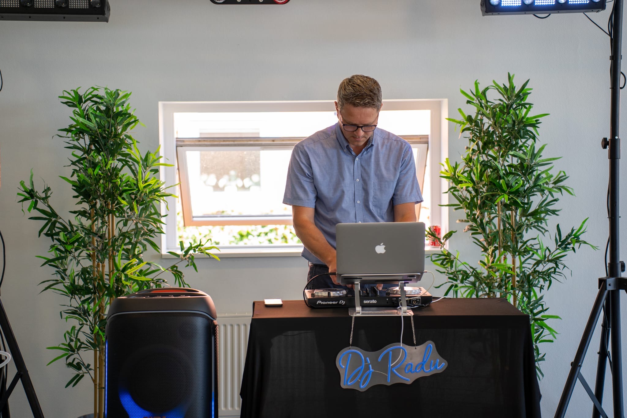 DJ Radu bag pladerne i et plantedekoreret rum, under neonskiltet 'DJ Radu'