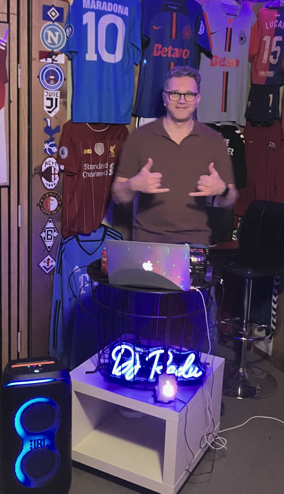 DJ Radu ved pulten med neonskiltet 'DJ Radu' og fodboldtrøjerne bag sig